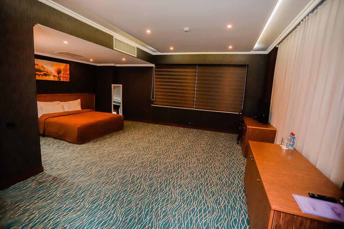 A hotel room with a bed, a desk, a chair, a window with blinds, and a wall-mounted TV.
