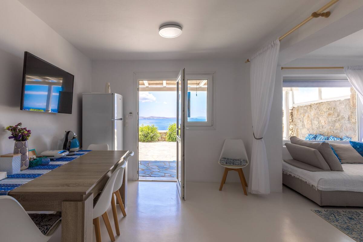 A modern, well-lit room with a dining area, a sofa, and a view of the sea.