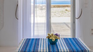 A room with a view of the sea through a glass door, a table with a patterned tablecloth, and a vase with flowers. - Sugar Blue (Mykonos)