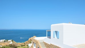 A coastal building with a white exterior and blue shutters, overlooking the sea. - Sugar Blue (Mykonos)