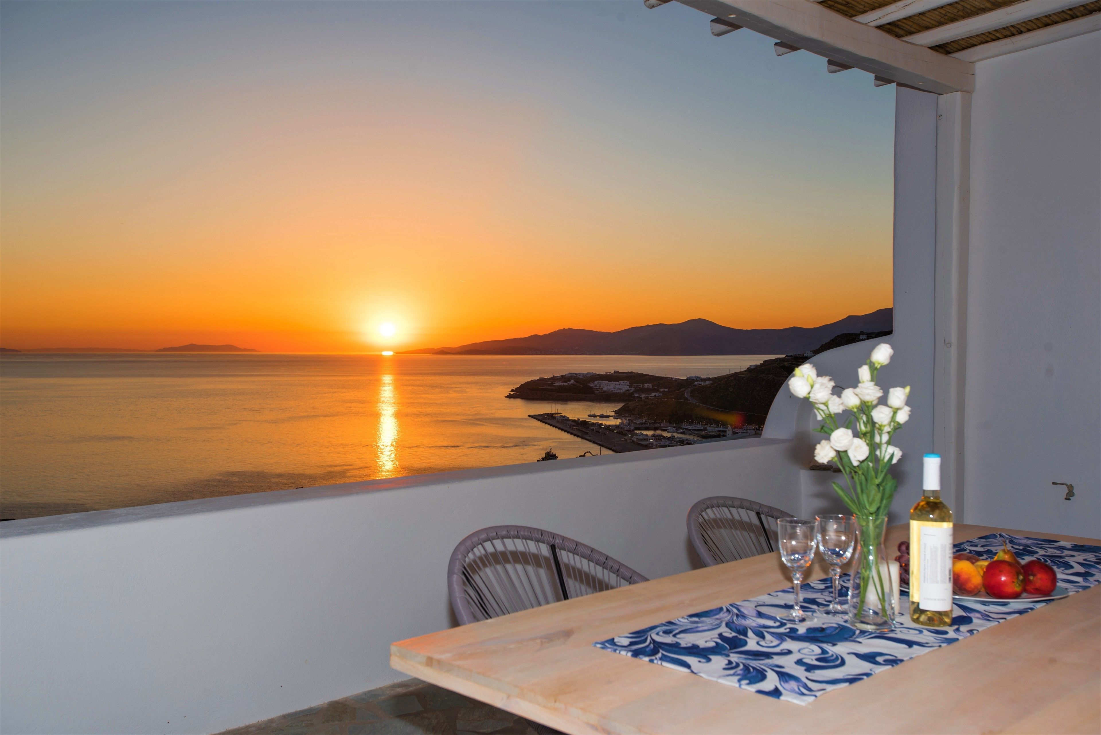 A dining area with a table set for two, overlooking a sunset over the sea.