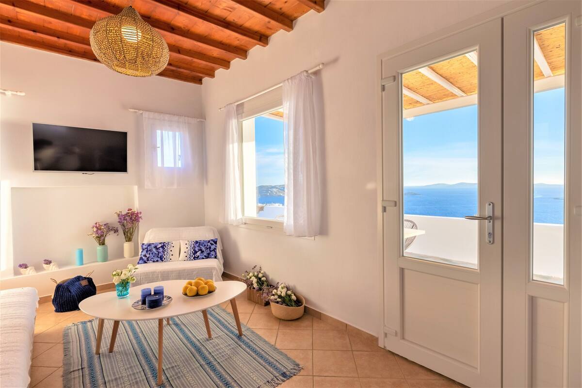A cozy room with a sofa, a TV, a table with candles, and a view of the sea.