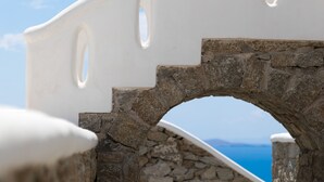 A stone archway with a white balustrade and a view of the sea in the background. - Sugar Blue (Mykonos)