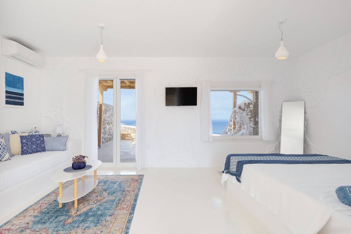 A bedroom with a bed, a sofa, a TV, and a view of the sea.