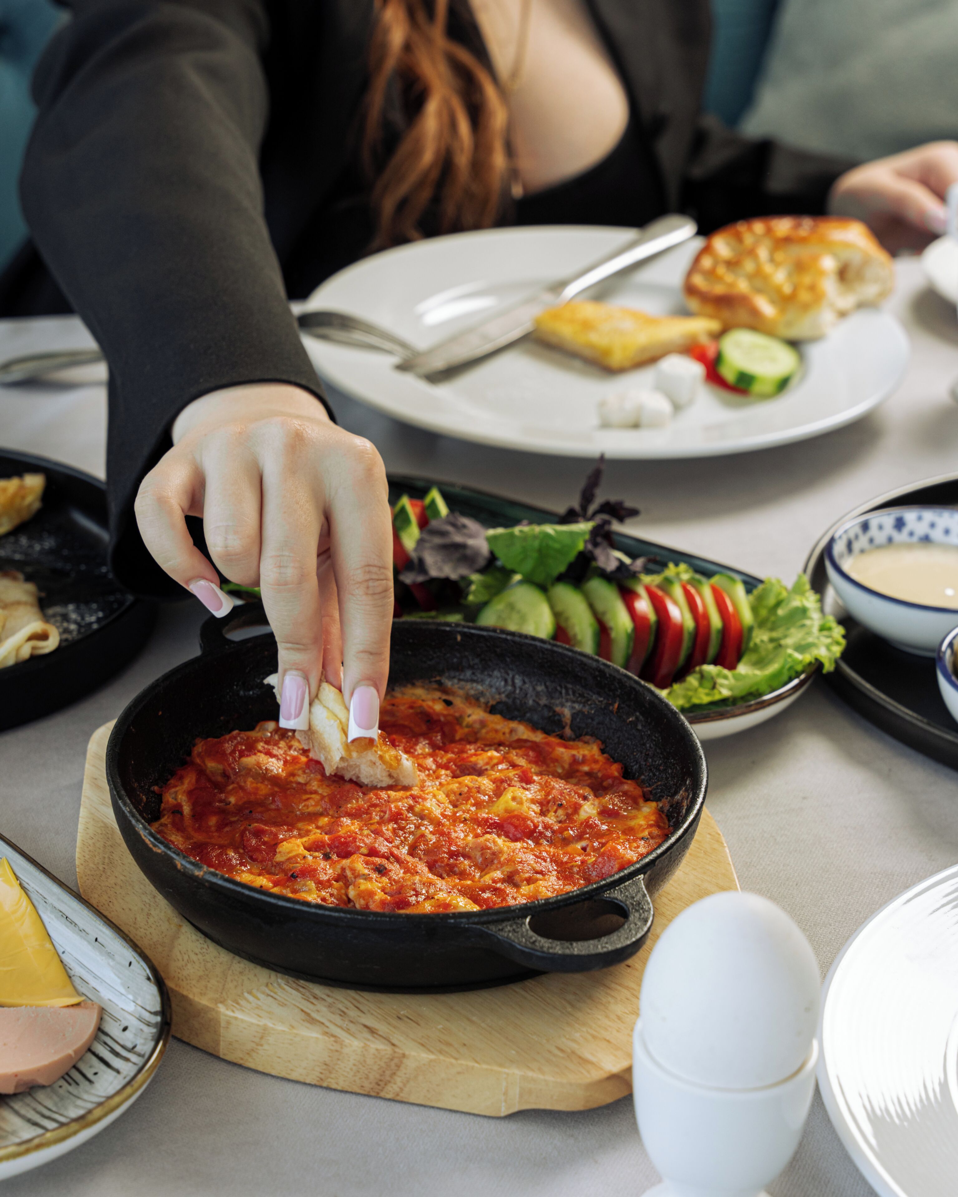Een eettafel met diverse gerechten, waaronder een braadpan met rode saus, een bord met salade en andere soorten eten.