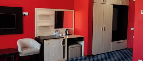 A hotel room with a checkered floor, a bed with towels, a desk with a mirror, a chair, and a wardrobe.