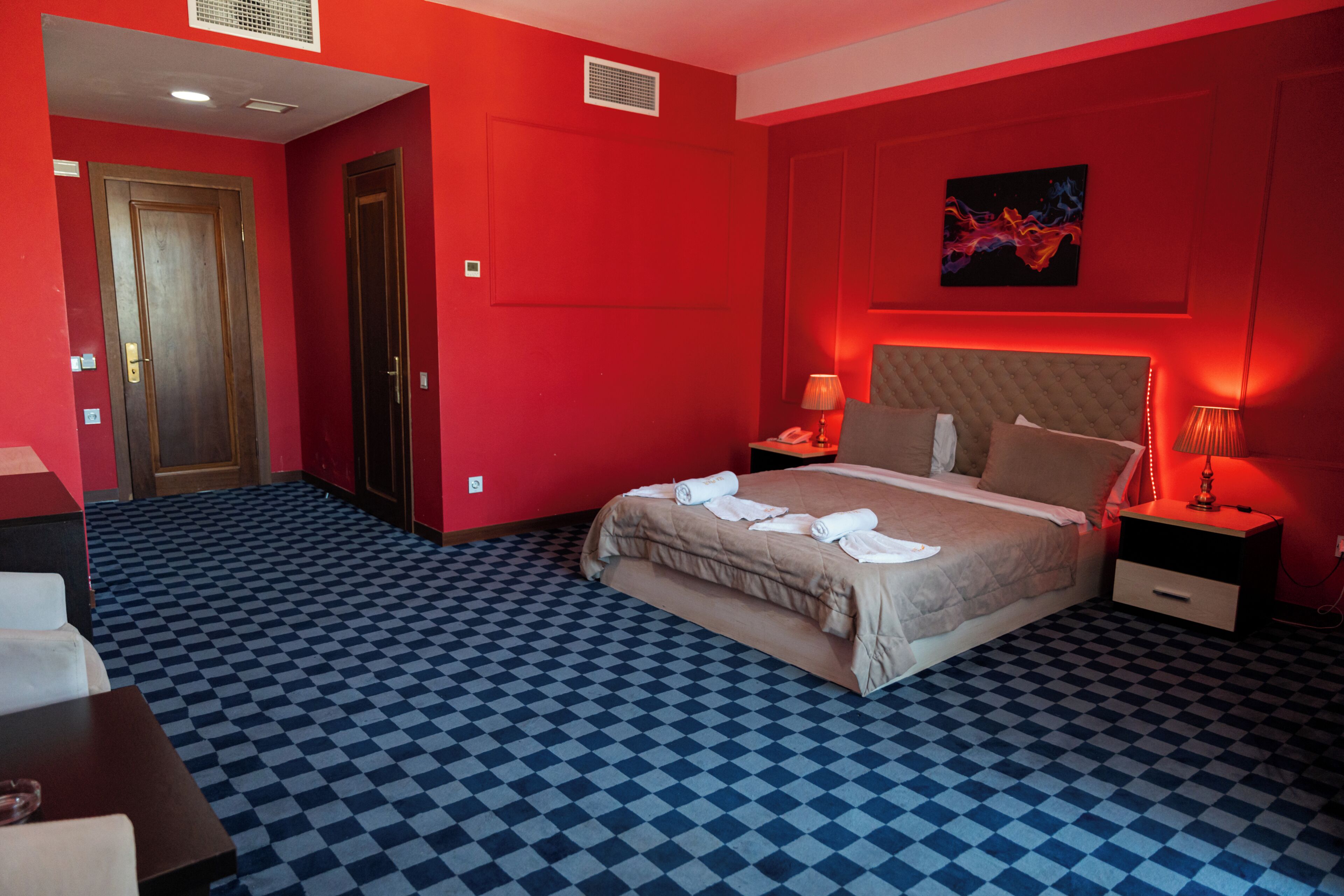 Una habitación de hotel con suelo a cuadros, una cama con toallas, una mesita de noche y un cuadro en la pared.