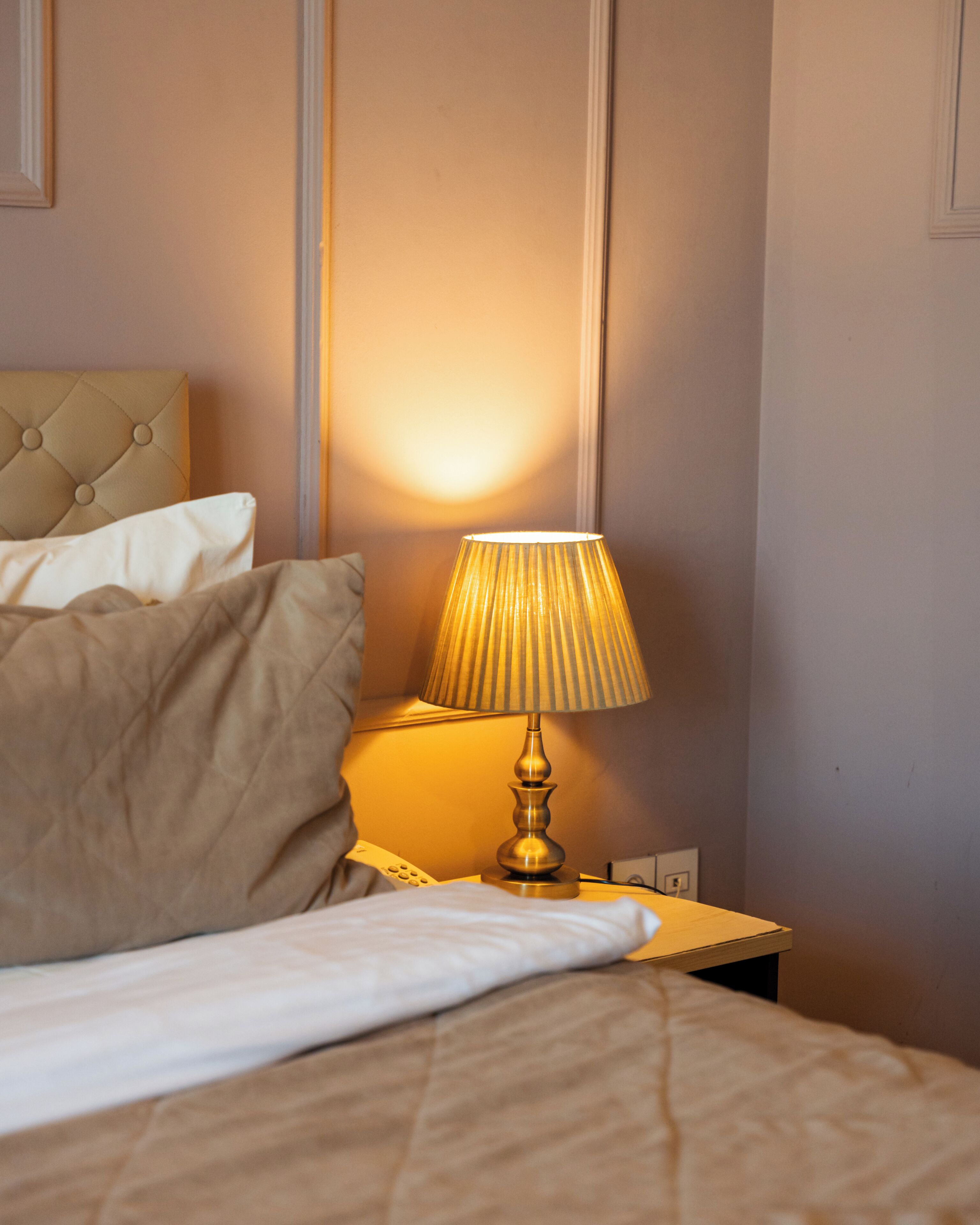 Een net opgemaakt bed met een hoofdbord, een bedlampje en een aan de muur bevestigde telefoon.