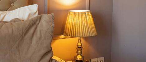 Een net opgemaakt bed met een hoofdbord, een bedlampje en een aan de muur bevestigde telefoon.
