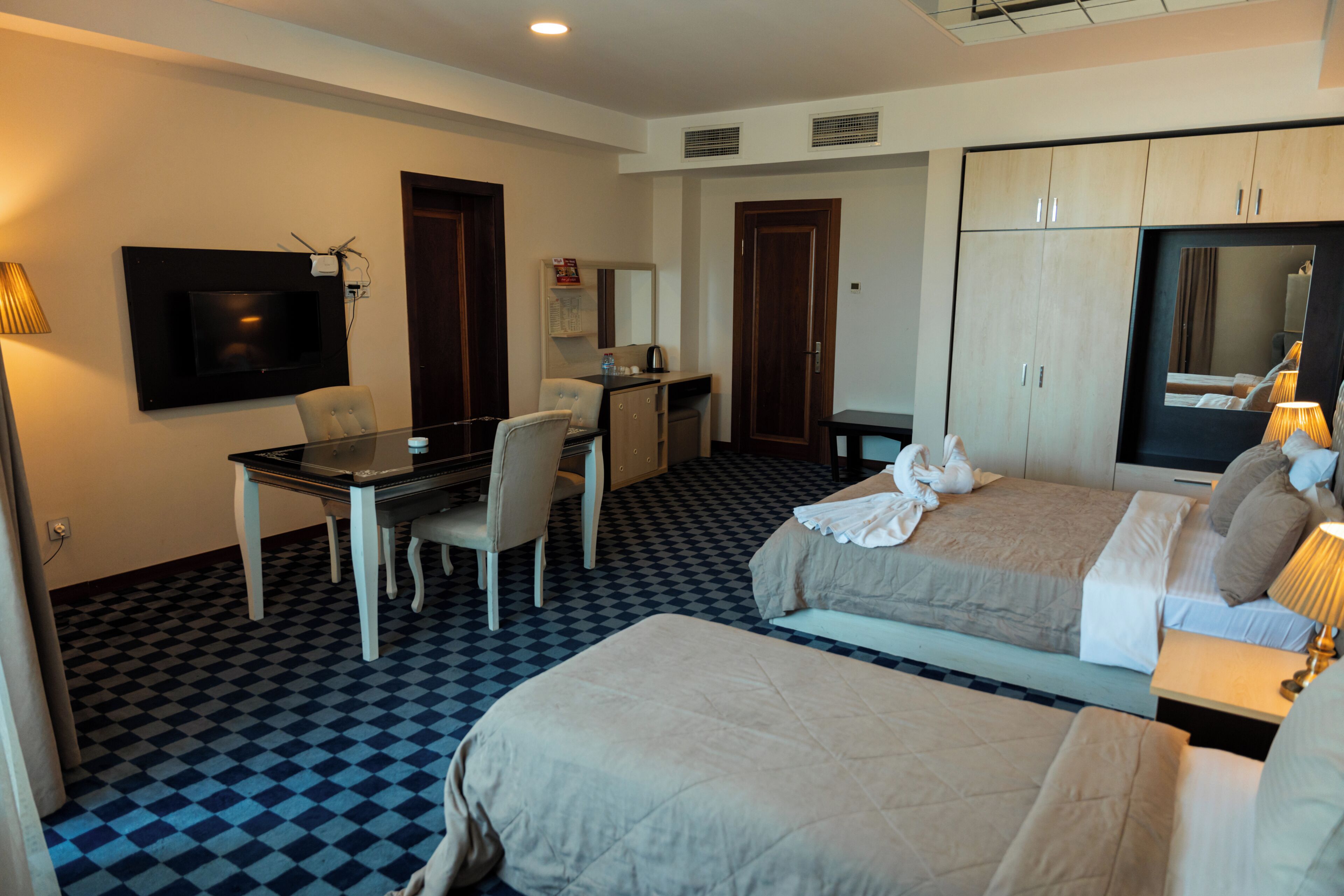 A hotel room with two beds, a desk, a chair, a TV, and a wardrobe.