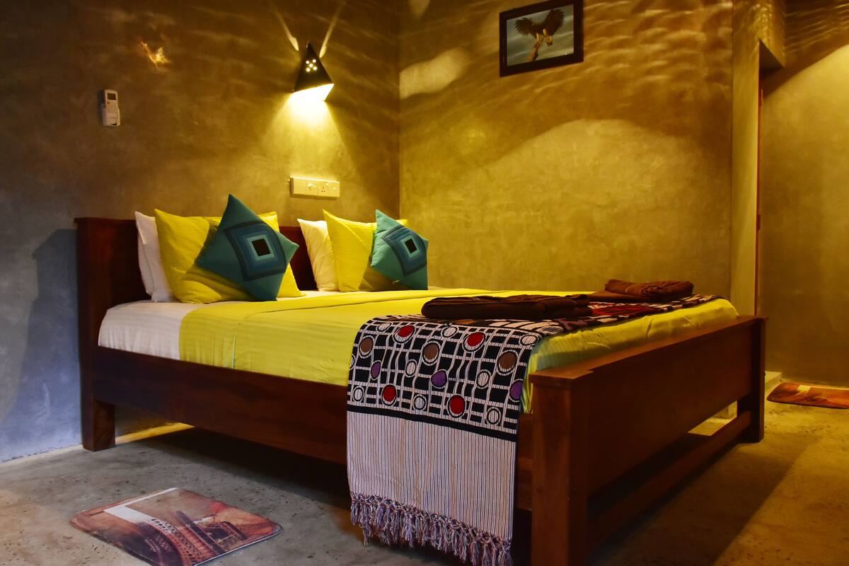 Un lit bien fait, avec une couvre-lit jaune, plusieurs oreillers et un plaid à motifs.