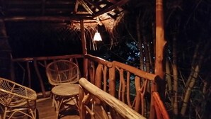 Une terrasse en bois, dotée de chaises en osier et d’une rambarde, entourée de structures en bambou.