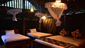 Une chambre avec deux lits, chacun étant agrémenté de draps blancs et d’une couverture à motifs. On y trouve des lampes suspendues et un lit à baldaquin recouvert d’un voile blanc transparent.