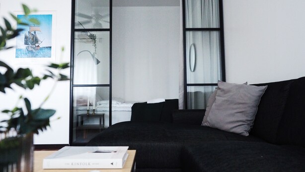 Een moderne woonkamer met een donkere bank, een klein tafeltje met een boek, en een schuifdeur die leidt naar een slaapkamer.