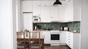 Een moderne keuken met witte kastjes, een magnetron, een kookplaat en een eettafel met stoelen.