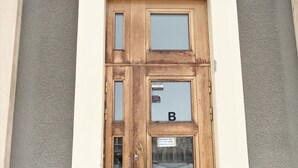 Een houten deur met een ruit en een bordje, in een gebouw met een betonnen fundering en een gestructureerde muur.