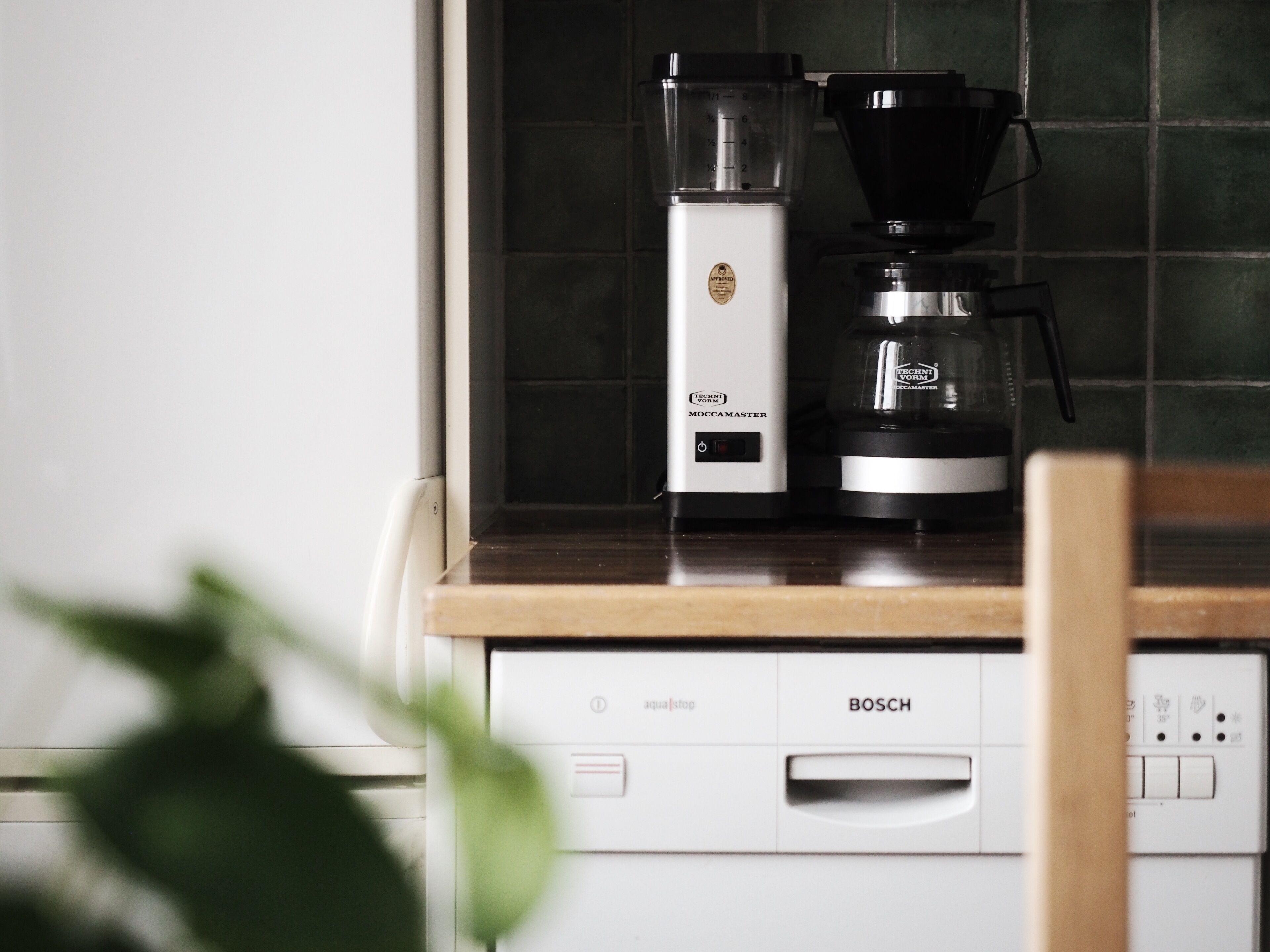 A kitchen with a coffee maker, a Bosch dishwasher, and a tiled backsplash.