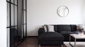 Een moderne woonkamer met een donkergrijze bank, een ronde spiegel en een houten salontafel.