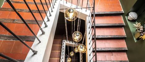 Una escalera de caracol con barandilla de metal, pared de ladrillo y lámpara colgante.