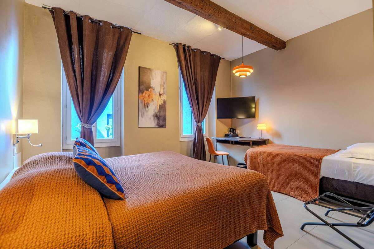 Een hotelkamer met twee bedden, een bureau, een televisie en een raam met gordijnen.