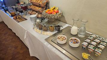 Uma mesa de buffet com diversos alimentos, incluindo frutas, doces e acompanhamentos.