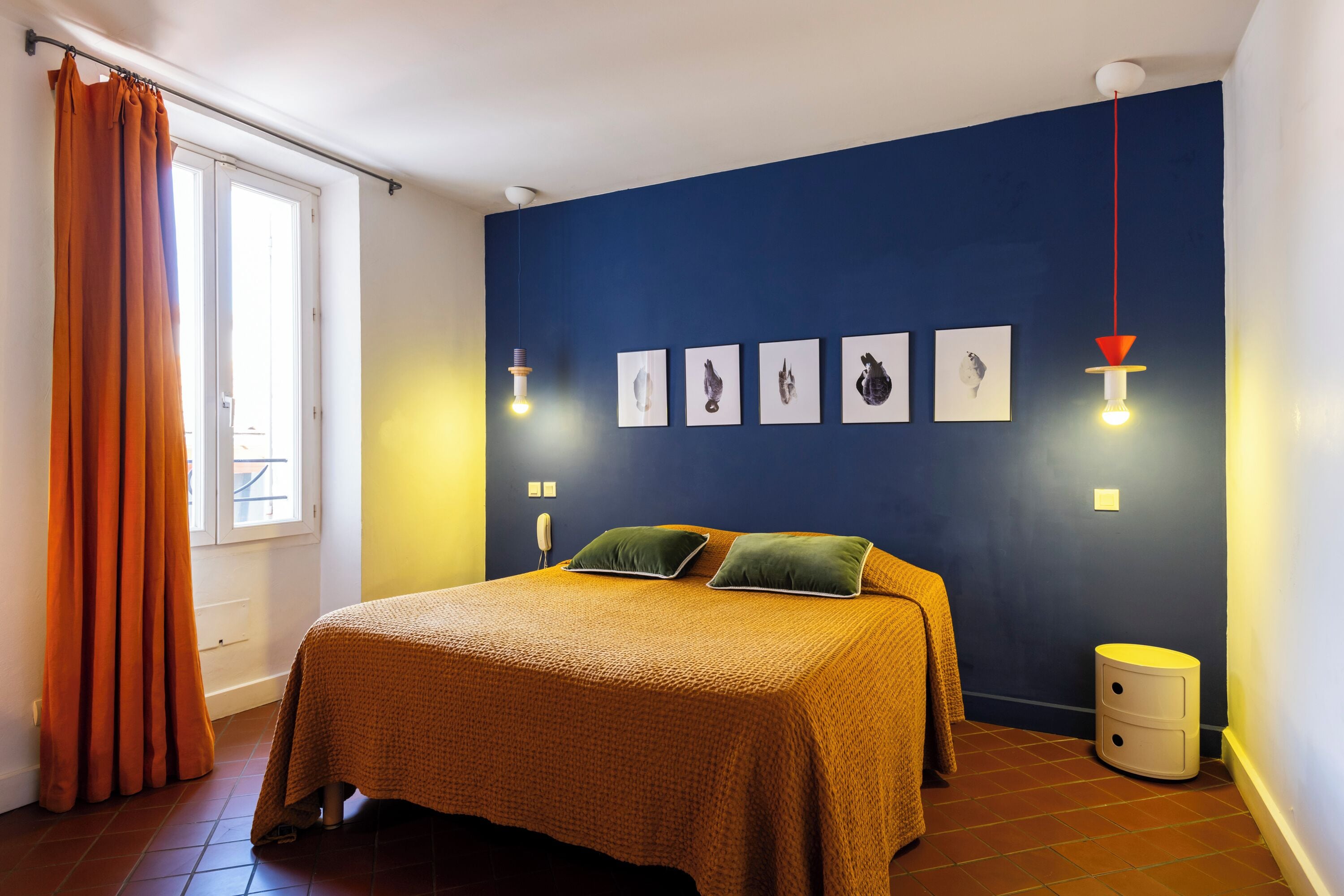 Un dormitorio con cama, mesita de noche, ventana con cortinas e iluminación en la pared.