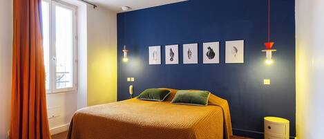 Un dormitorio con cama, mesita de noche, ventana con cortinas e iluminación en la pared.
