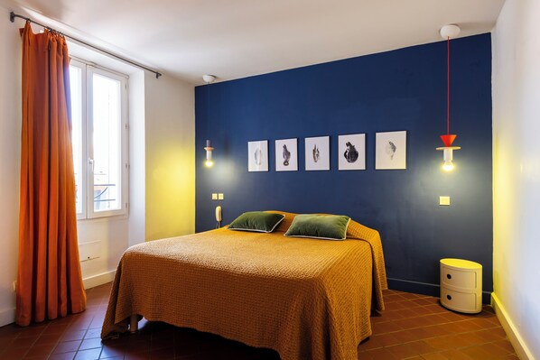 A bedroom with a bed, a nightstand, a window with curtains, and wall-mounted lights.