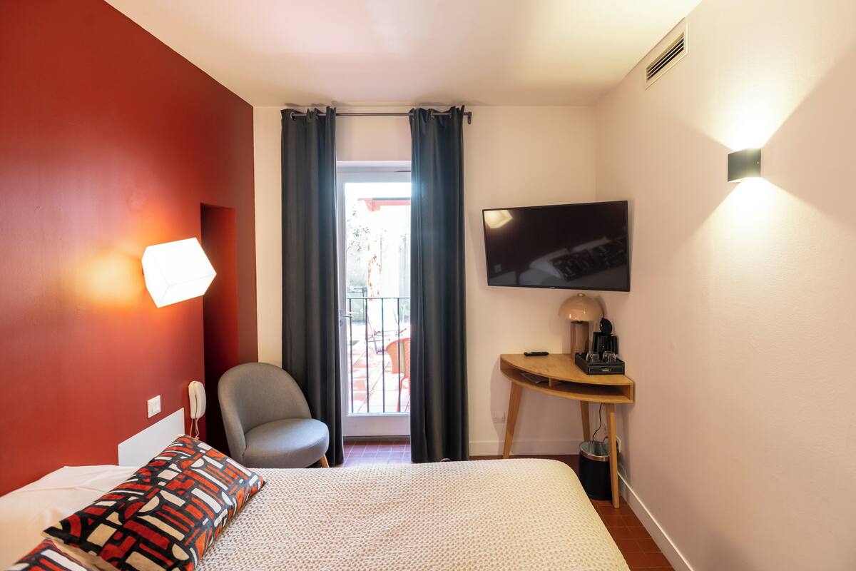Een hotelkamer met een bed, een stoel, een bureau met een televisie en een raam met gordijnen.