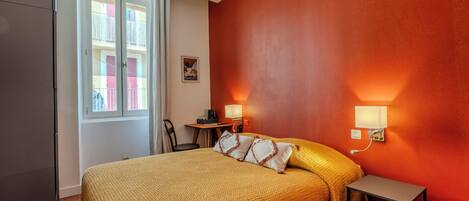 A room with a bed, a desk, two wall-mounted lamps, and a window.