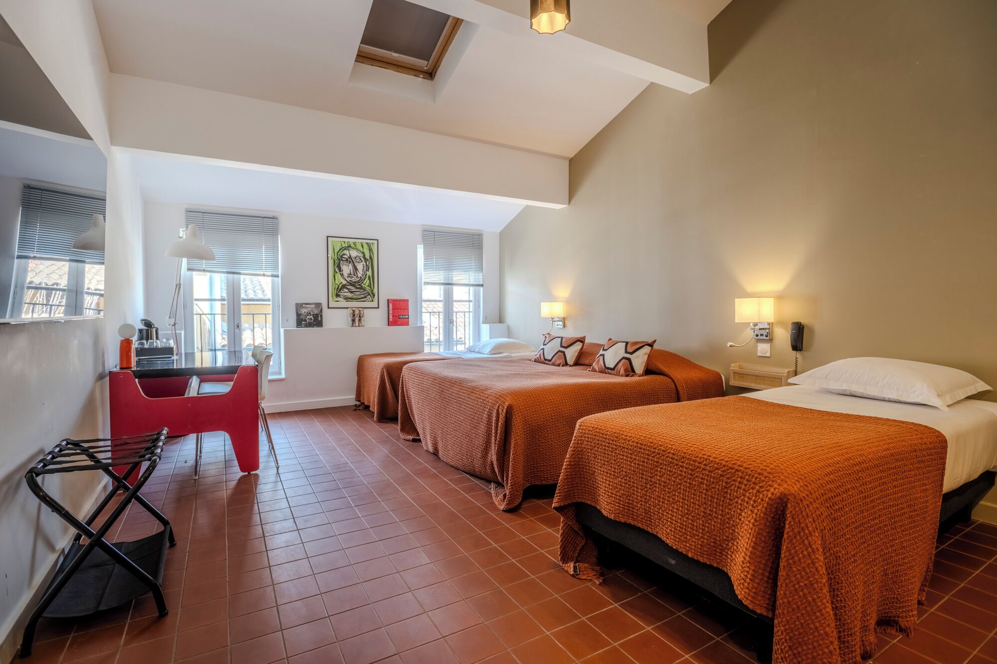 Quarto de hotel com duas camas, uma escrivaninha, uma cadeira e uma janela com persianas.