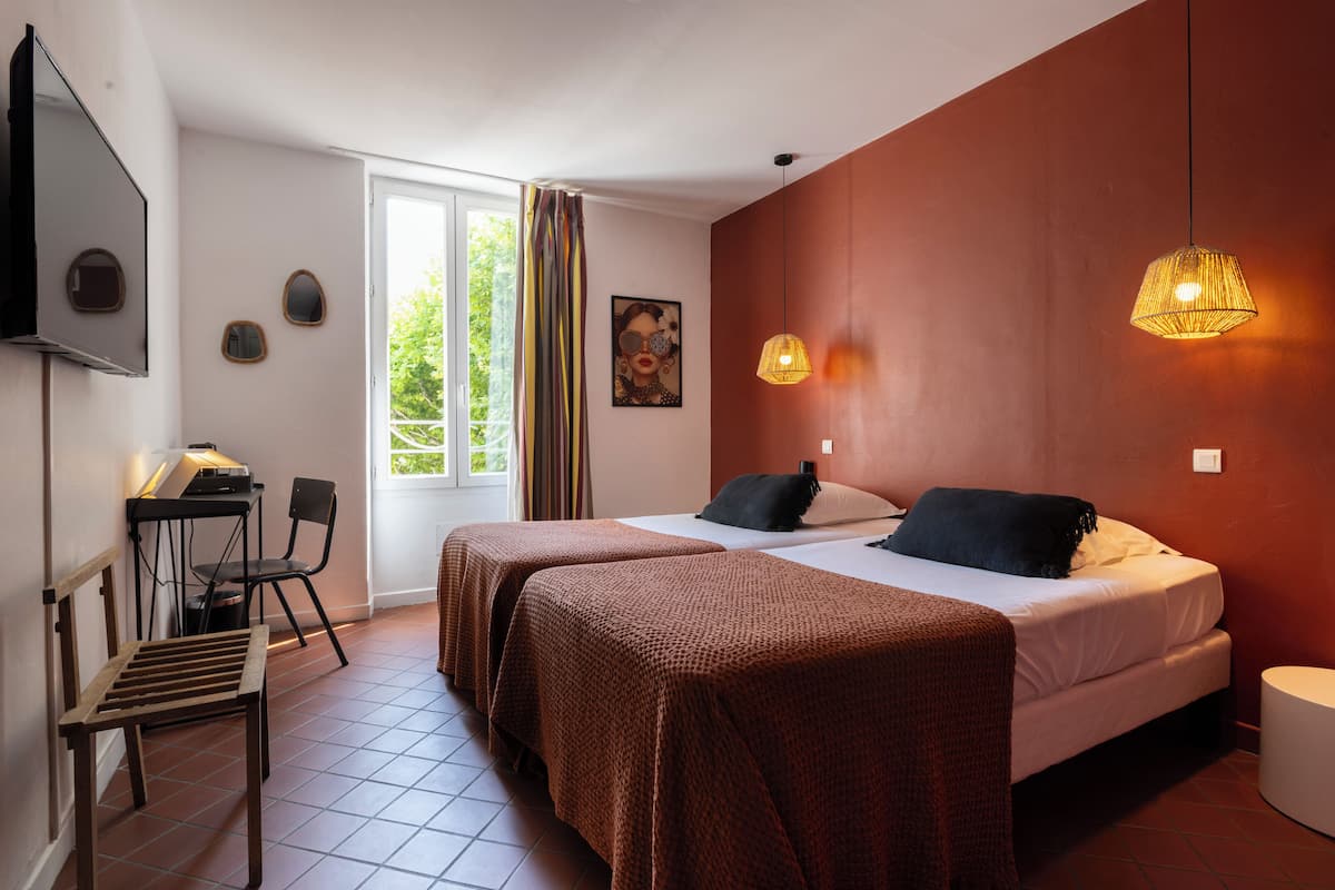 Een hotelkamer met twee bedden, een bureau met stoel, een televisie en een groot raam met gordijnen.