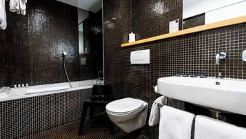 A modern bathroom with a black tiled wall, a white sink, a bathtub, and a toilet.