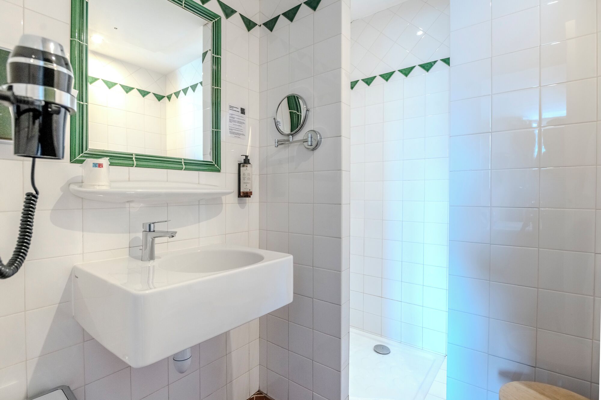 A bathroom with a white sink, a mirror, a hairdryer, and a shower.