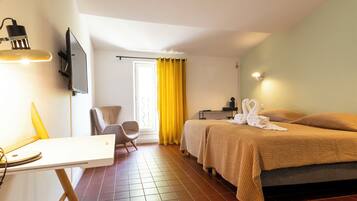 A hotel room with a bed, a desk, a chair, a TV, and a window with curtains.