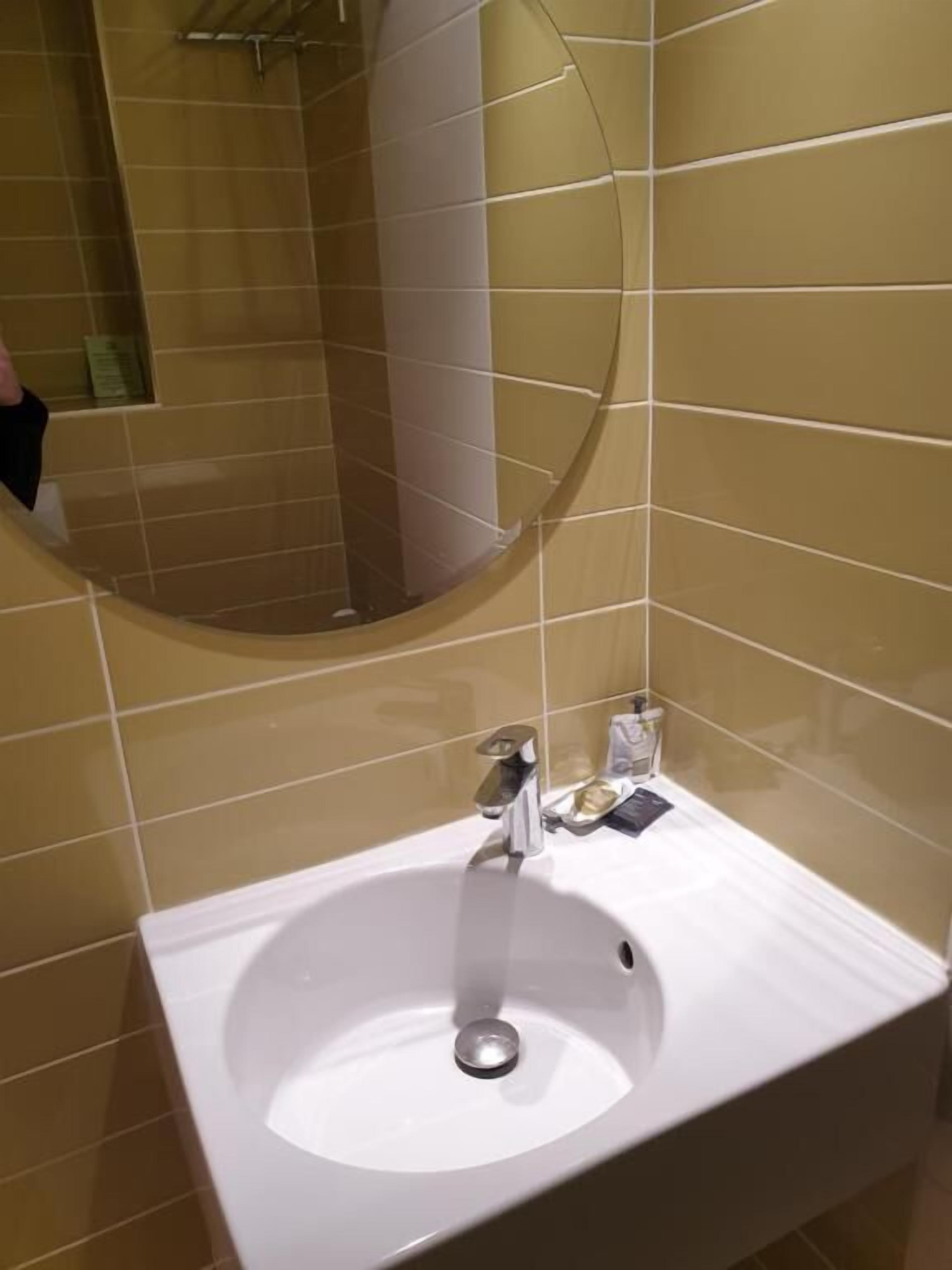 A bathroom with a white sink, a mirror, and beige tiled walls.