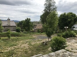 Paisagem rural com edifícios de pedra, um campo gramado e uma árvore grande.
