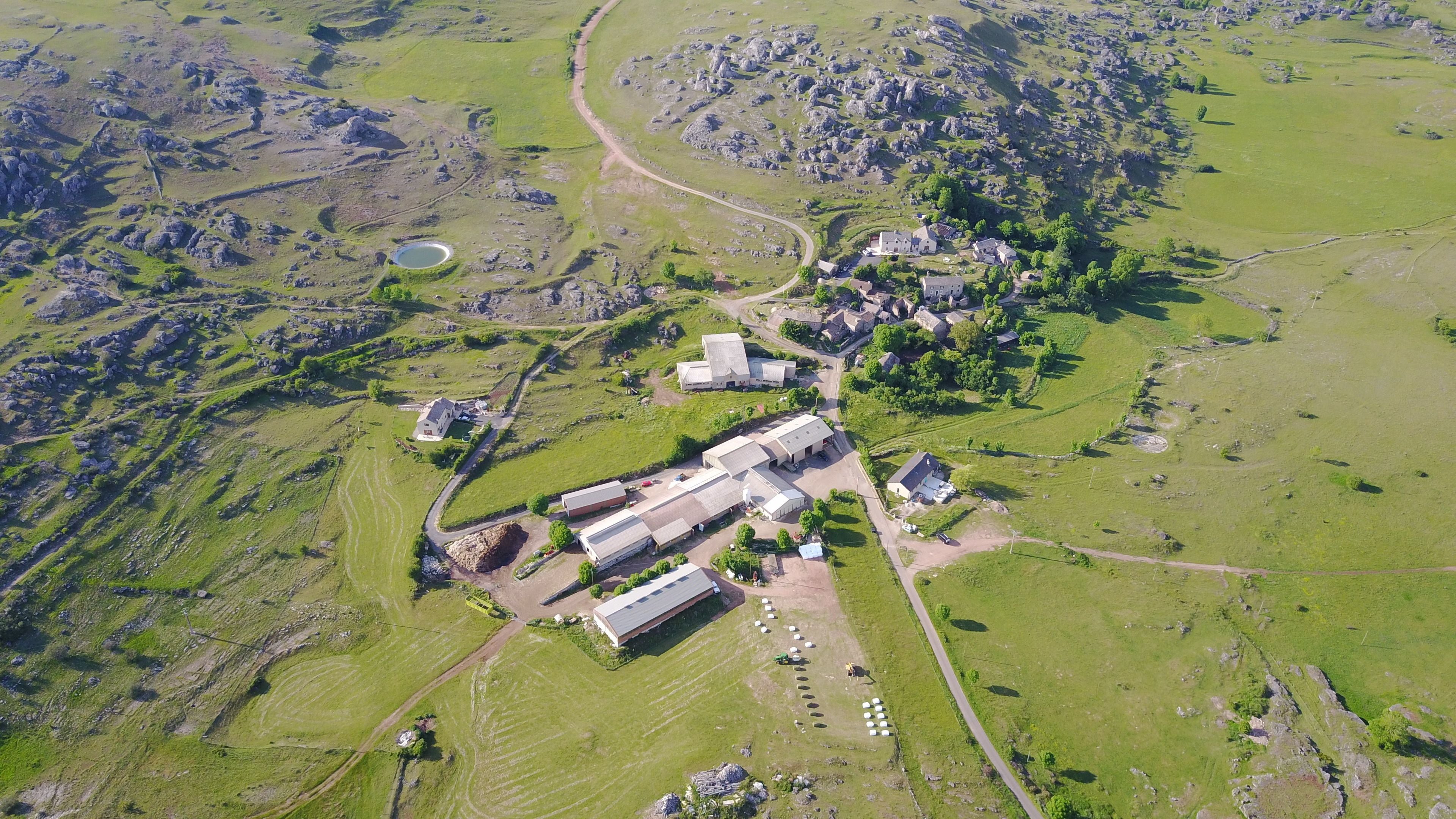 An aerial view of a rural area with scattered buildings, a large open field, and a winding road.