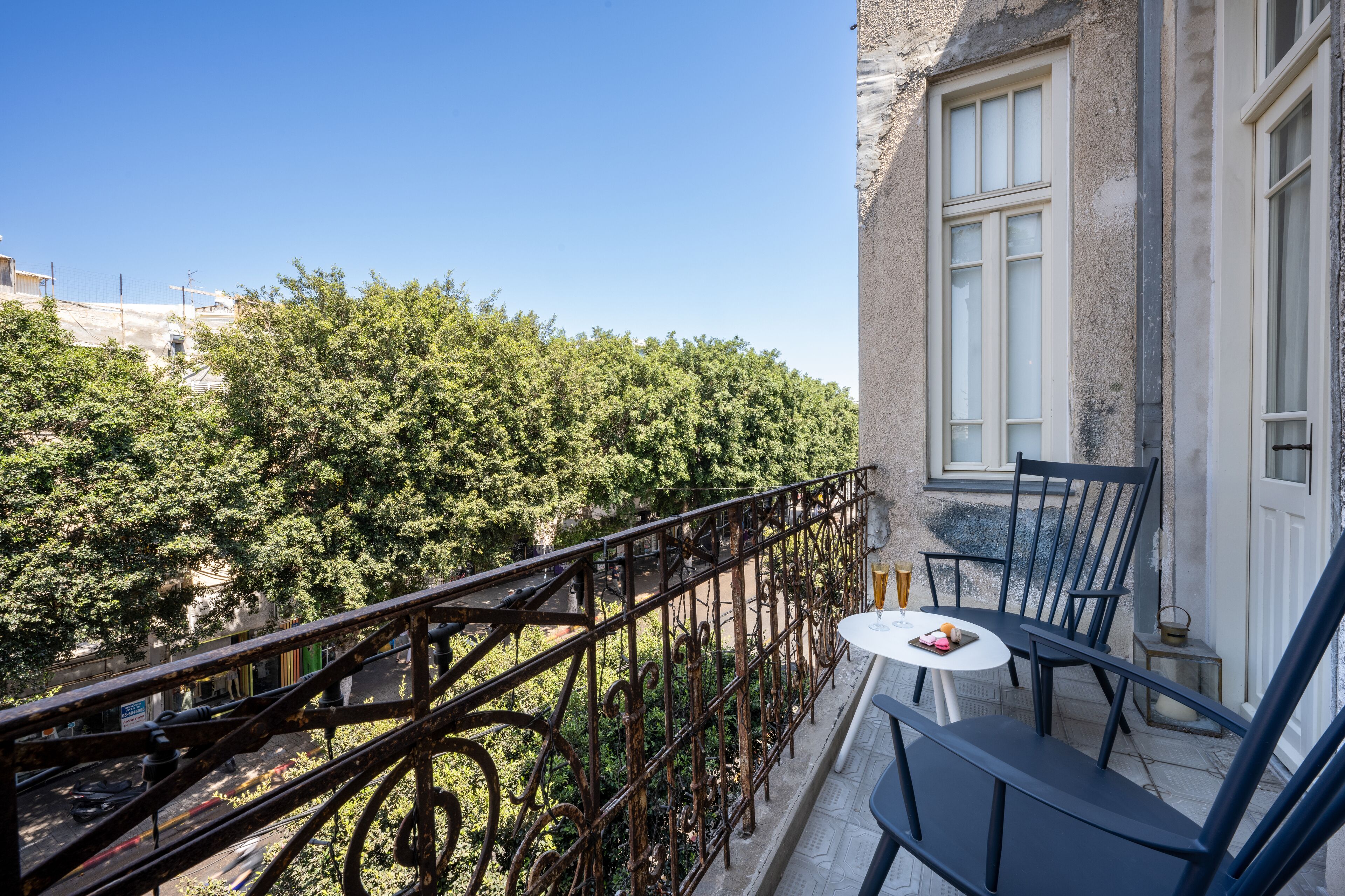 A balcony with a view of trees, a table with chairs, and a window.