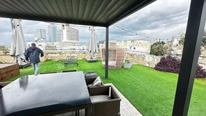 Um pátio externo com mesa e cadeiras, gramado e vista para a cidade.