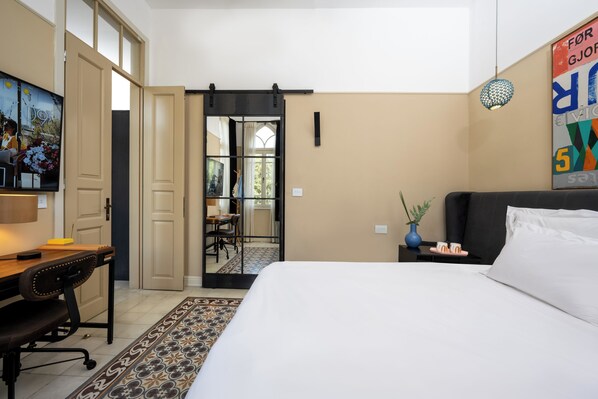 Quarto de hotel com uma cama, escrivaninha, cadeira, televisão, porta e janela.