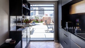 A modern kitchen with a view of the cityscape, a dining area with a table and chairs, and a balcony with a wicker chair. - Assemblage Boutique (Tel Aviv)