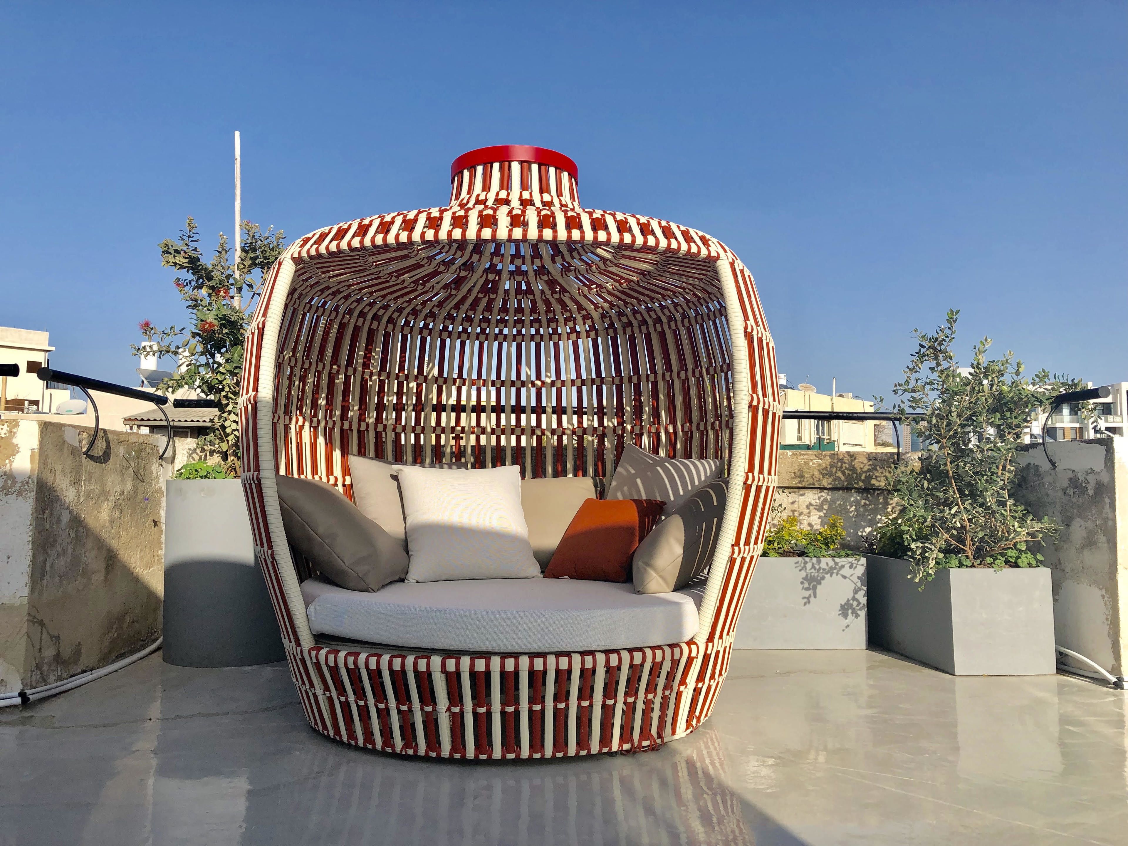 A circular, woven outdoor seating area with cushions and a red top.