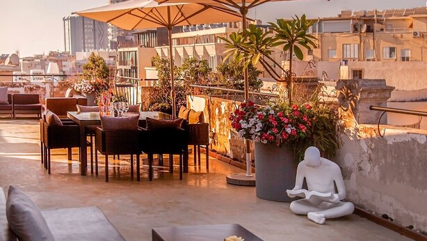 A rooftop terrace with outdoor seating, umbrellas, and a statue. - Assemblage Boutique (Tel Aviv)