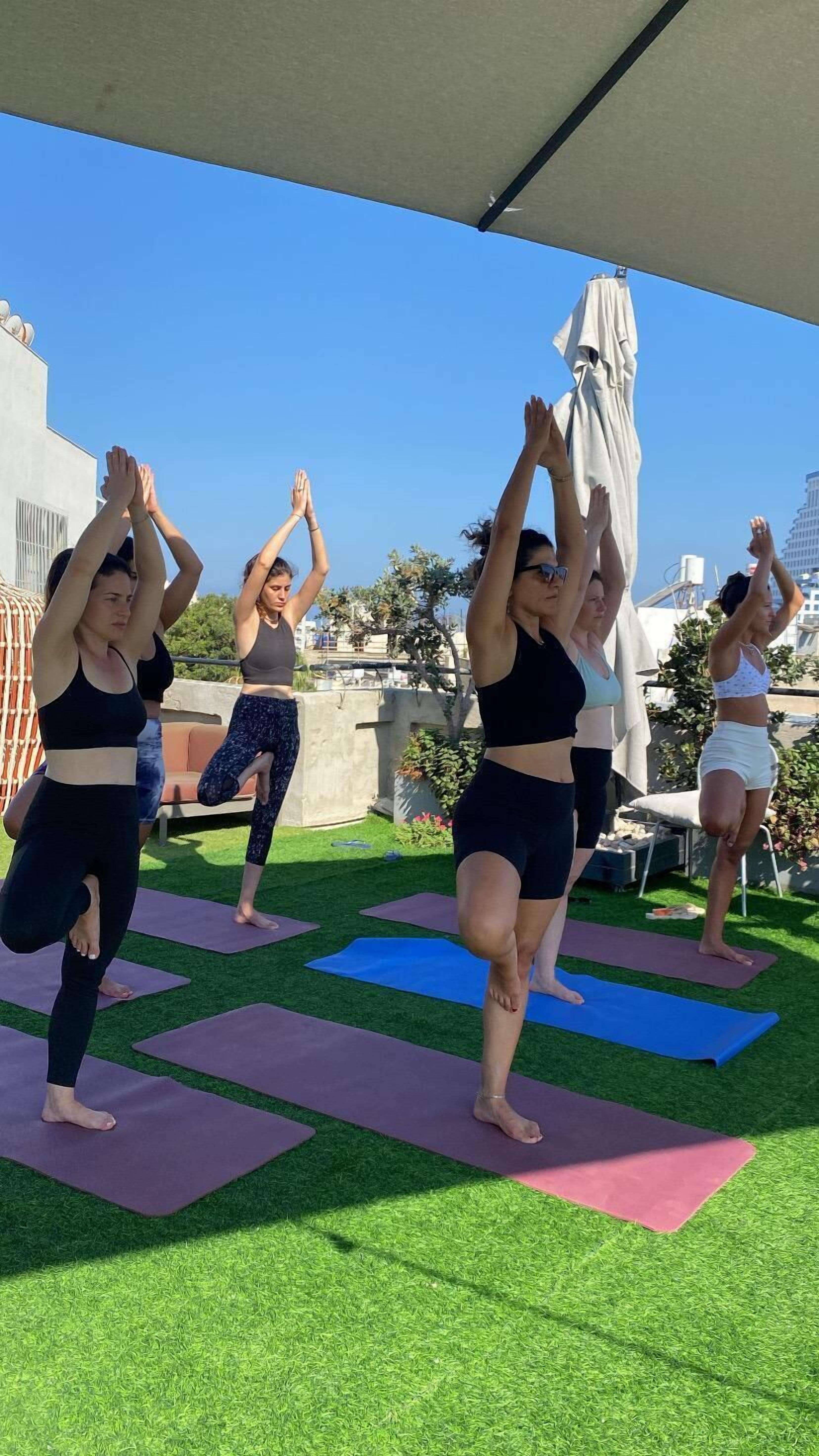 A group of people performing yoga on outdoor mats under a canopy.