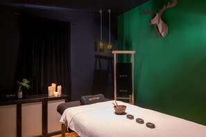 Uma sala de spa com mesa de massagem, velas, uma planta e um enfeite de cabeça de veado.