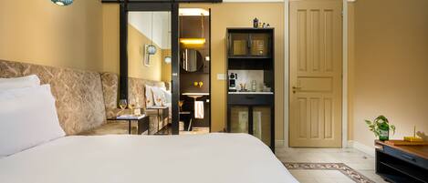 A hotel room with a large bed, a desk with a chair, a wardrobe, and a door leading to a bathroom.