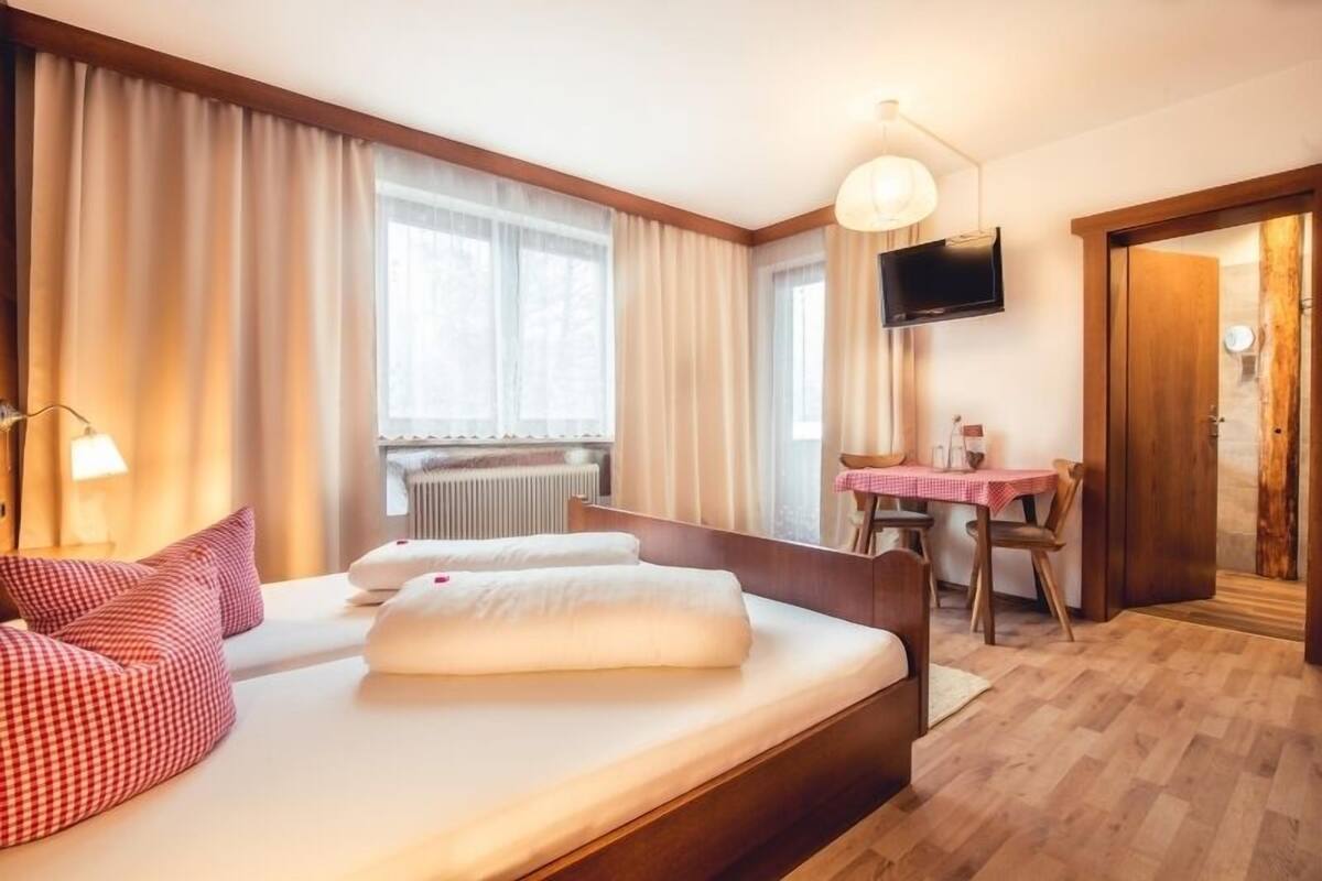 A hotel room with a bed, a table, a chair, a TV, and a window with curtains.