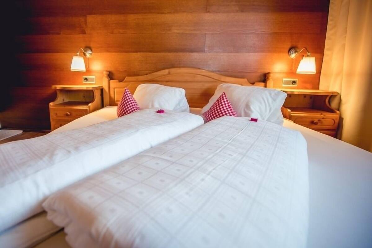 A double bed with white linens and checkered pillows, wooden headboard, and bedside lamps.
