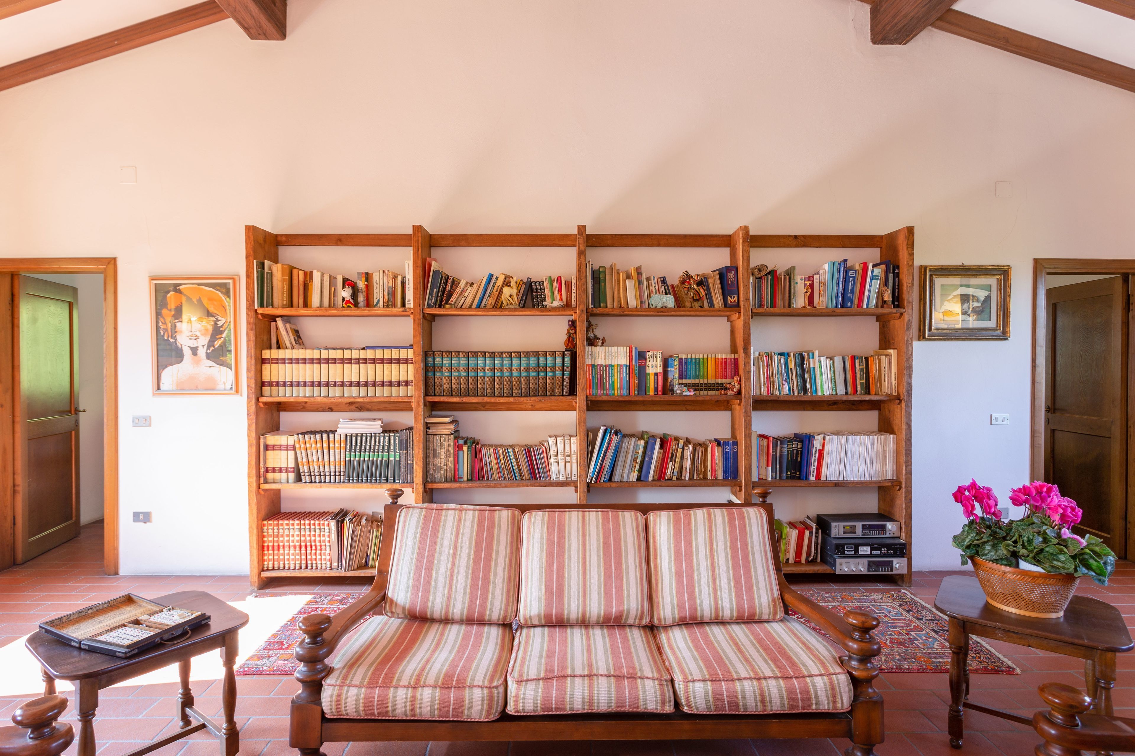 Un salon chaleureux avec un canapé à rayures, une bibliothèque en bois remplie de livres, une petite table avec une radio et une plante en pot.